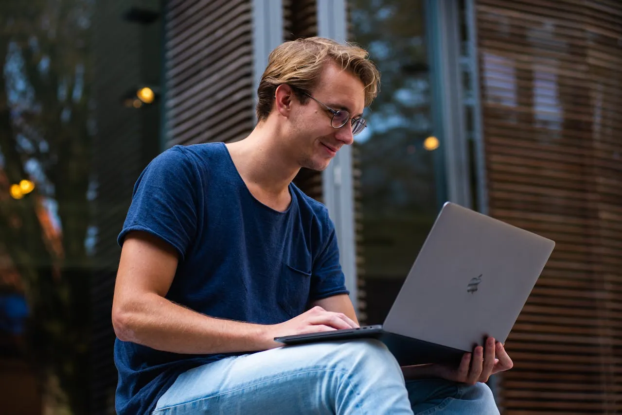 A man sitting on a bench using a laptop computer.