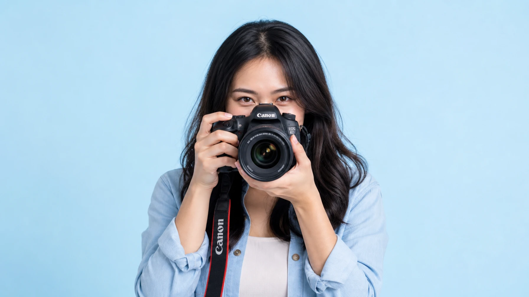 Malaysian social media content creator holding a Canon camera on a light blue studio background